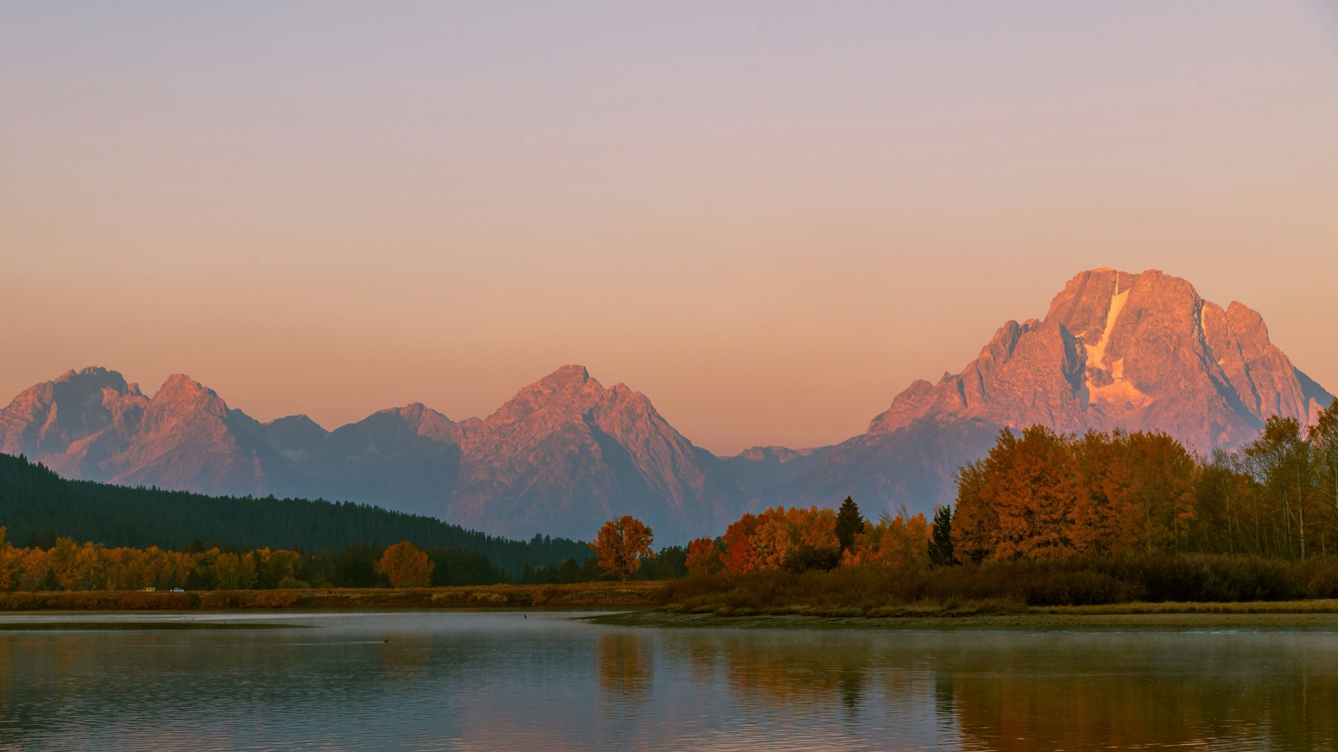 Sunrise light on Mount Moran and the Teton Range with autumn cottonwoods above the Snake River reflection at Oxbow Bend.